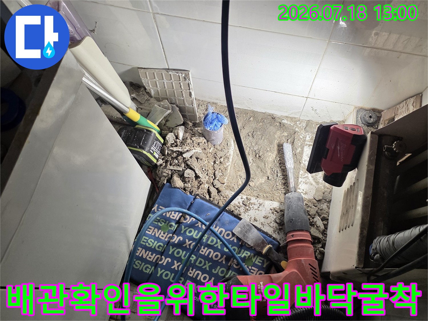 붉은색 전동 드릴을 사용하여 바닥의 타일과 콘크리트를 파내고 있는 누수 공사 모습