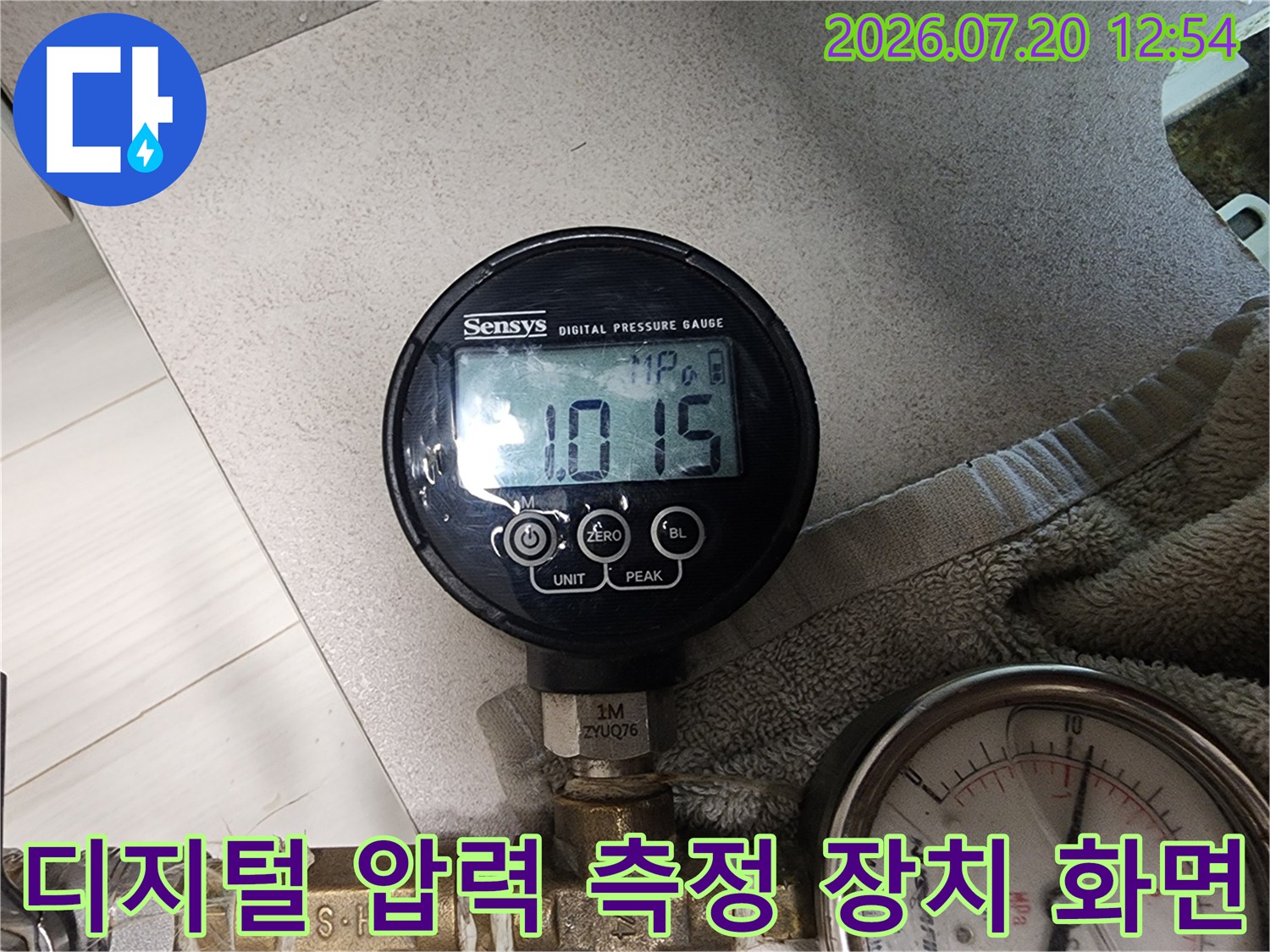 황동색 배관 연결부에 설치되어 현재 압력을 숫자로 보여주는 디지털 게이지