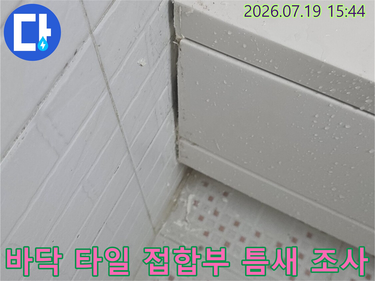 화장실 바닥의 흰색 타일과 구조물이 만나는 지점의 마감 상태를 확인하는 모습
