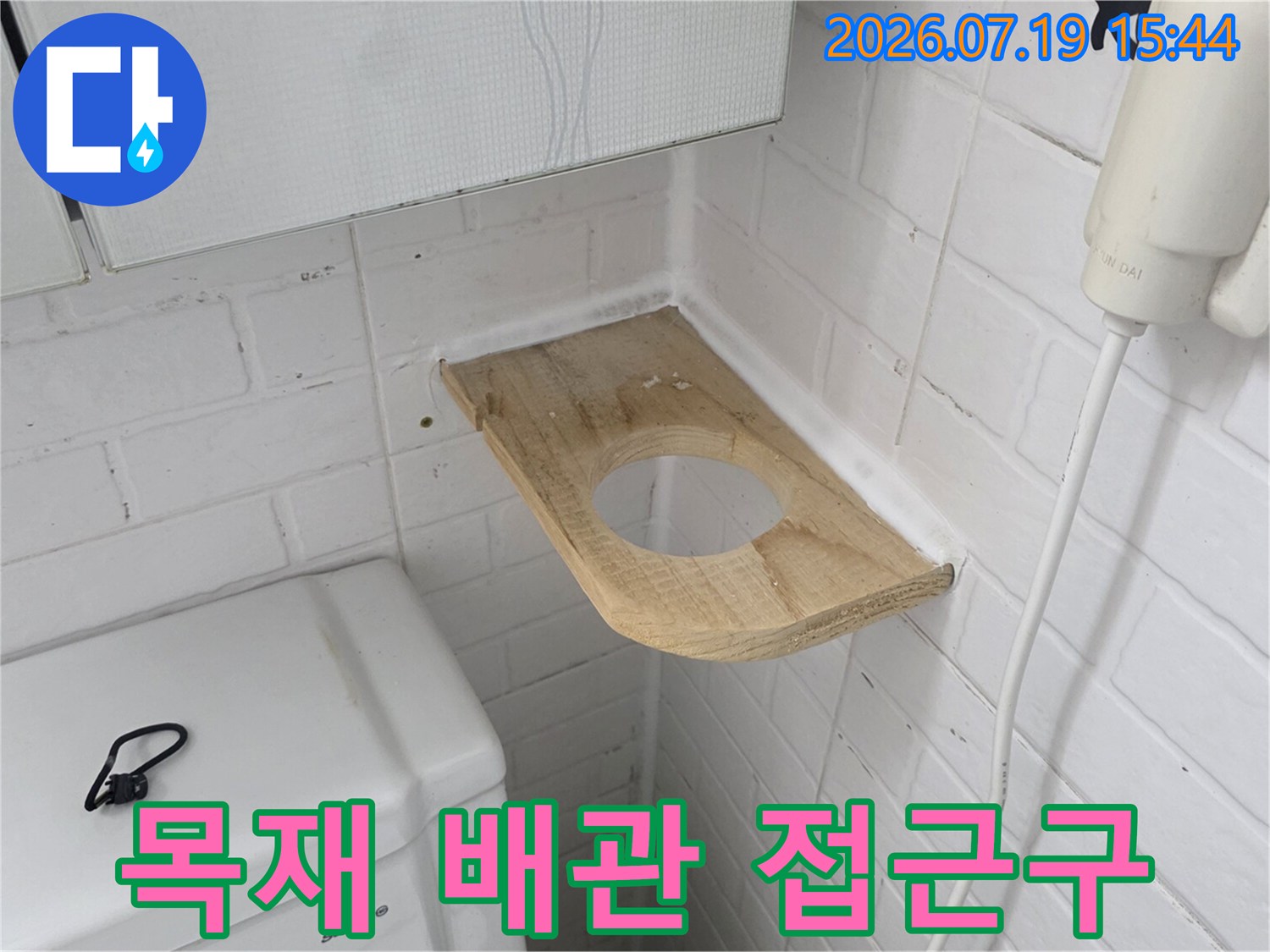 흰색 타일 벽과 변기 사이-원형 구멍이 있는 나무판이 설치된 사진