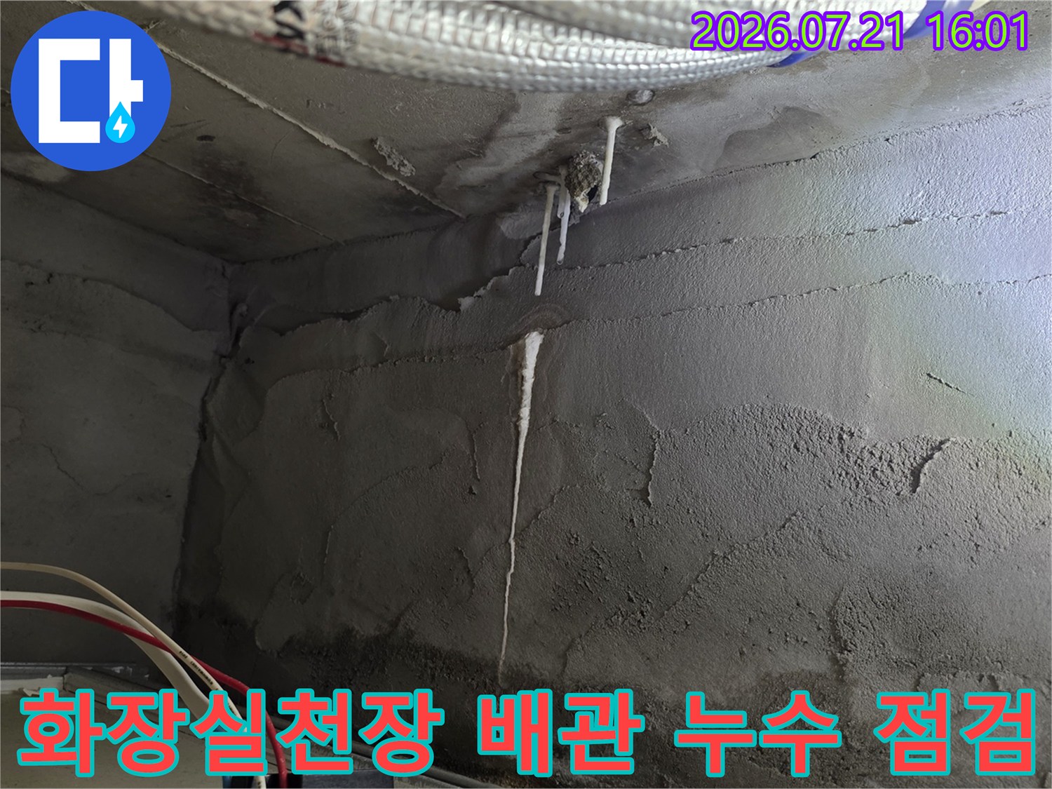 회색 콘크리트 벽면과 하얀색 보온재로 감싸진 배관이 노출된 화장실 천장 내부 모습