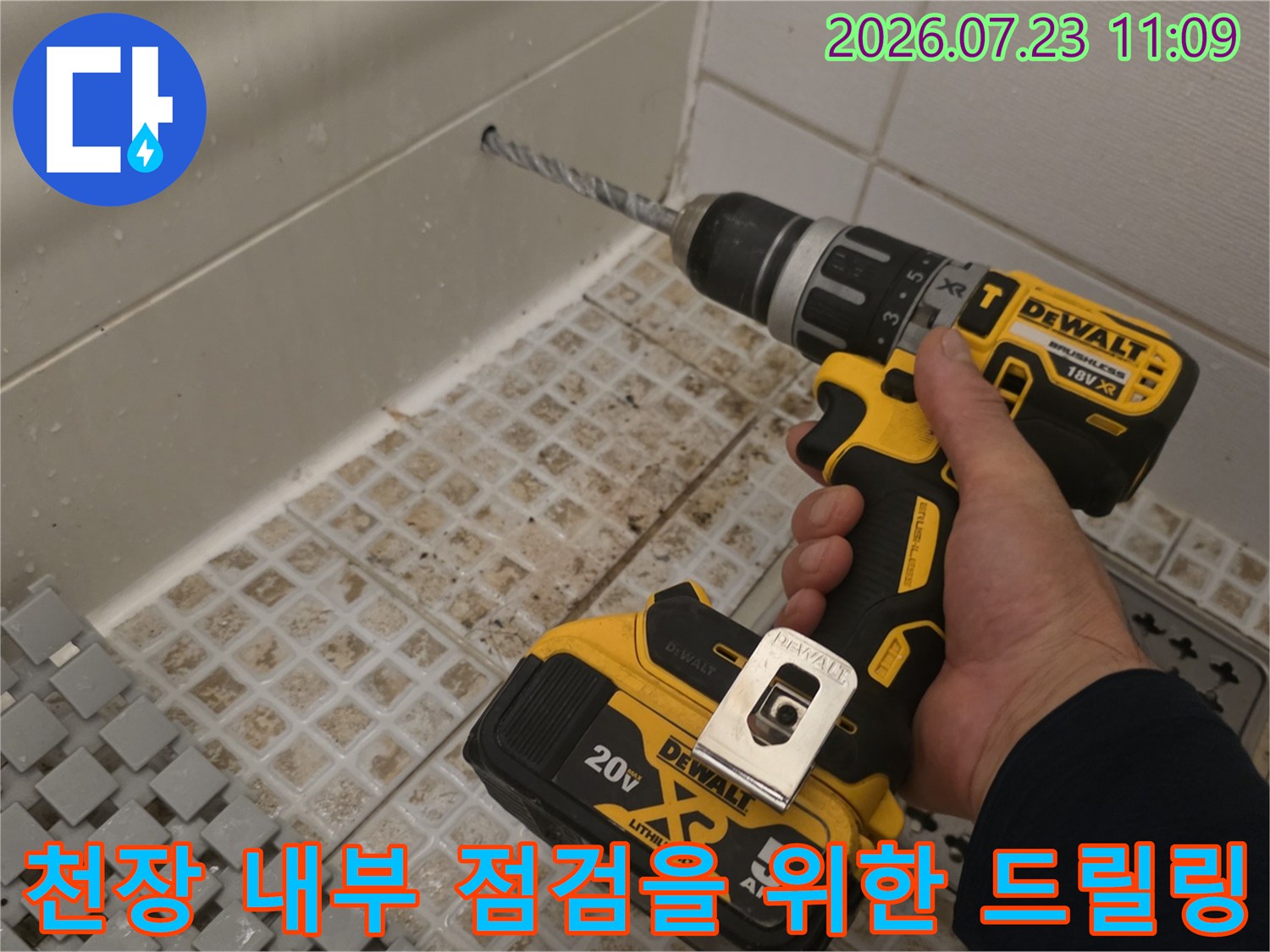 노란색 전동드릴로 화장실 천장의 흰색 마감재 부분을 타공하고 있는 모습