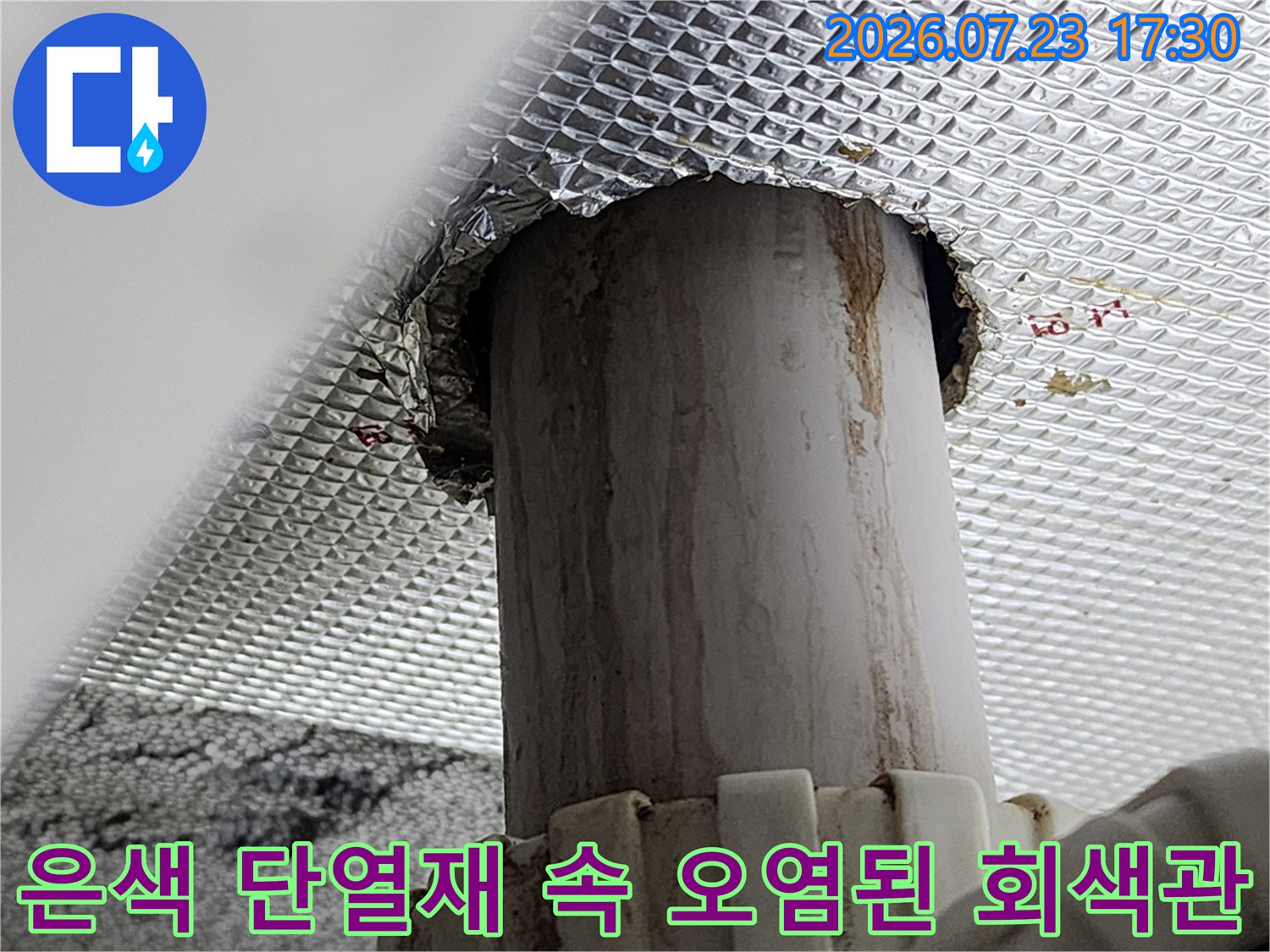 화장실 천장의 은색 반사 마감재 구멍을 통해 드러난 물때 낀 회색 하수 배관 사진