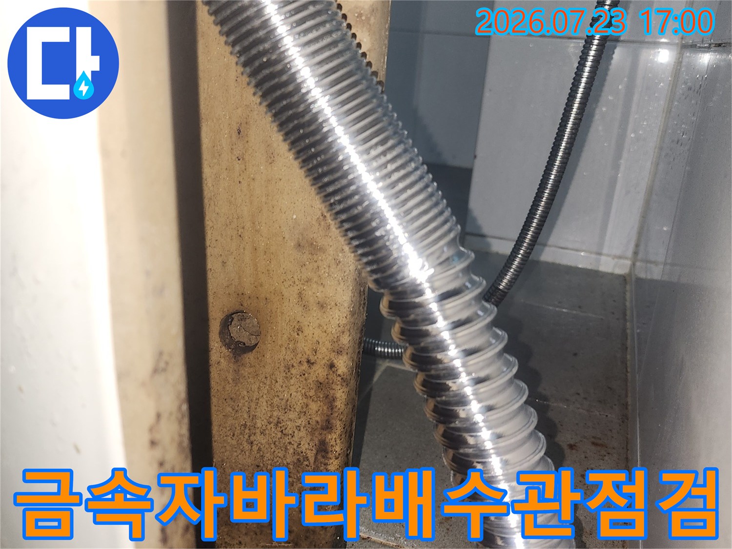 벽면 배출구에 연결된 은색 금속 자바라 호스와 주변의 오염된 벽체 모습