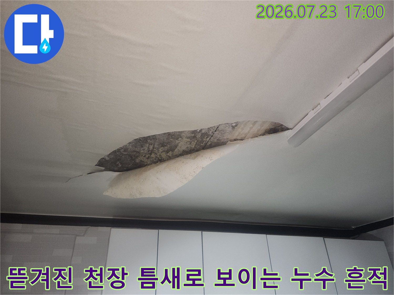 흰색 천장 마감재가 길게 찢어져 내부의 젖은 콘크리트 표면이 드러난 모습
