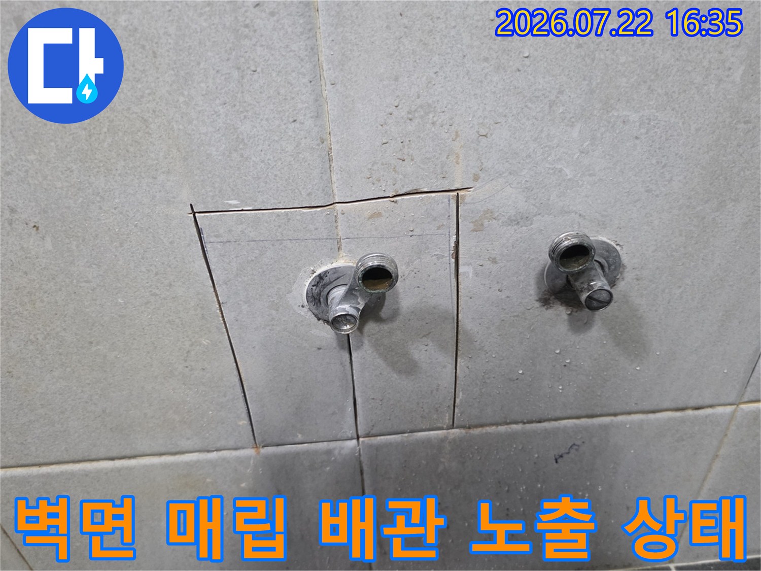 타일 벽면을 일부 제거하여 드러난 두 개의 금속 수도 배관 연결 부위