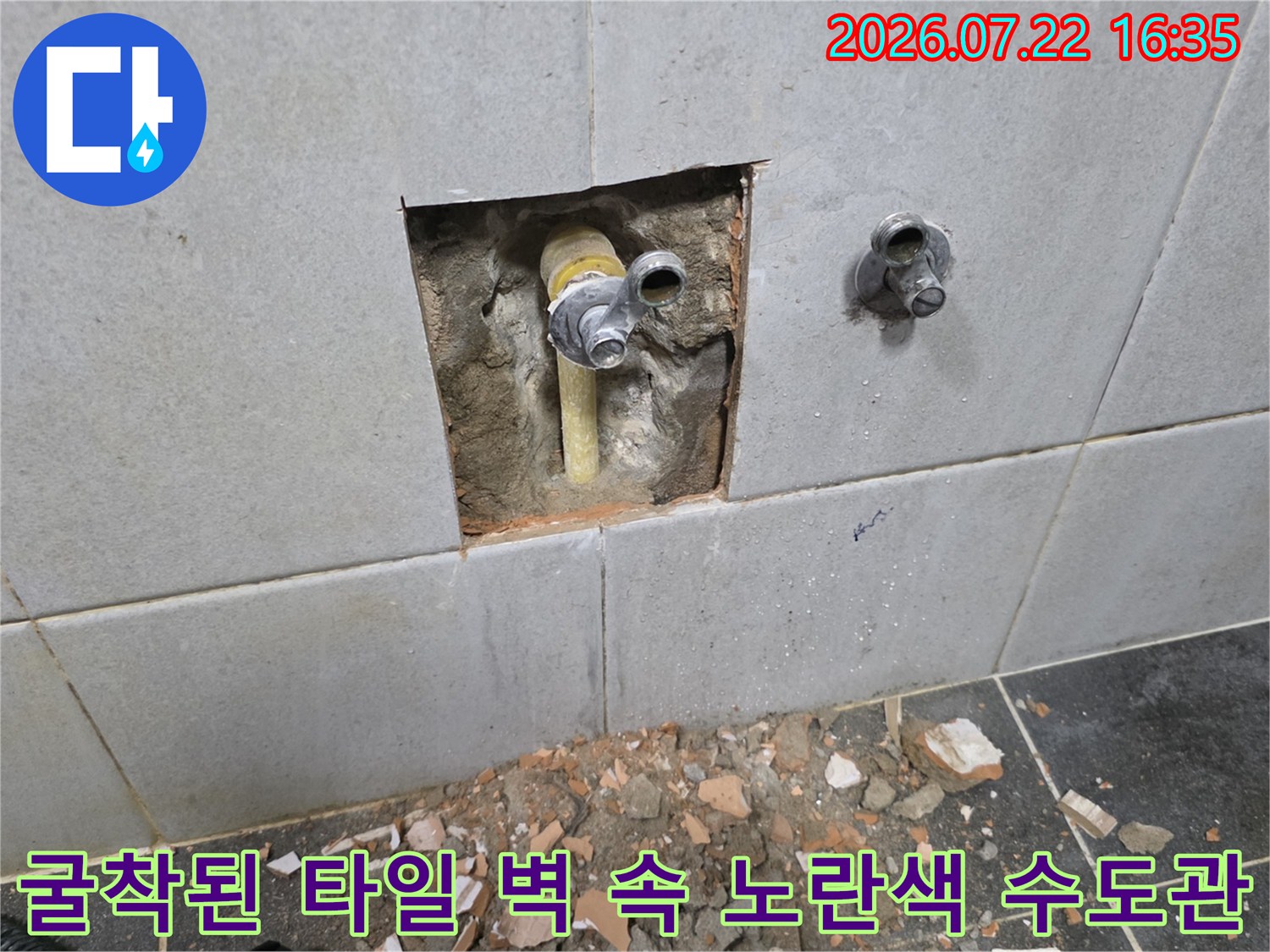 회색 타일 벽 속에 매립되어 있던 노란색 피피씨 배관-연결 부속이 드러난 장면