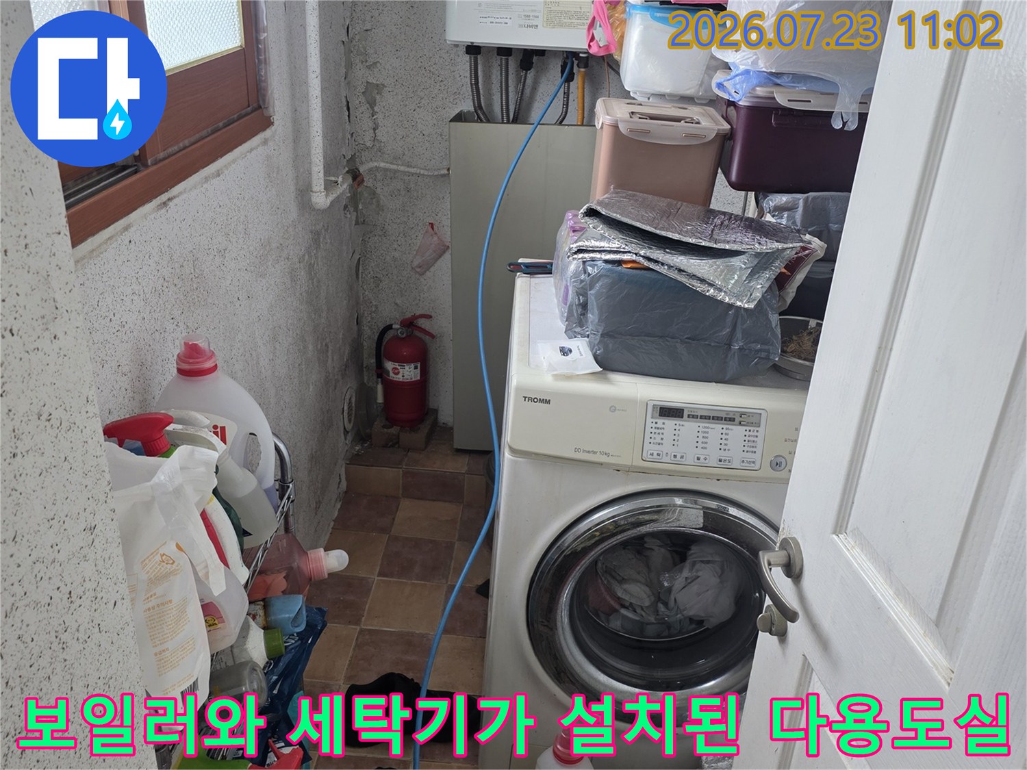 흰색 보일러와 드럼세탁기가 설치되어 있고 바닥에 세제들이 놓인 공간