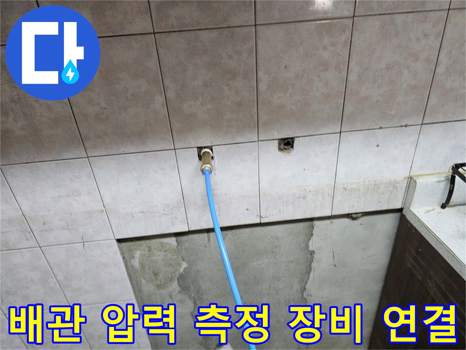 벽면 타일 사이 배관에 연결된 파란색 호스 이미지