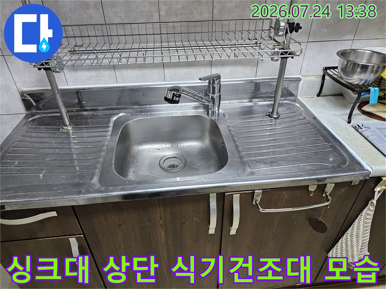 은색 스테인리스 싱크볼과 수도꼭지 그리고 상부 건조대가 보이는 주방 전경