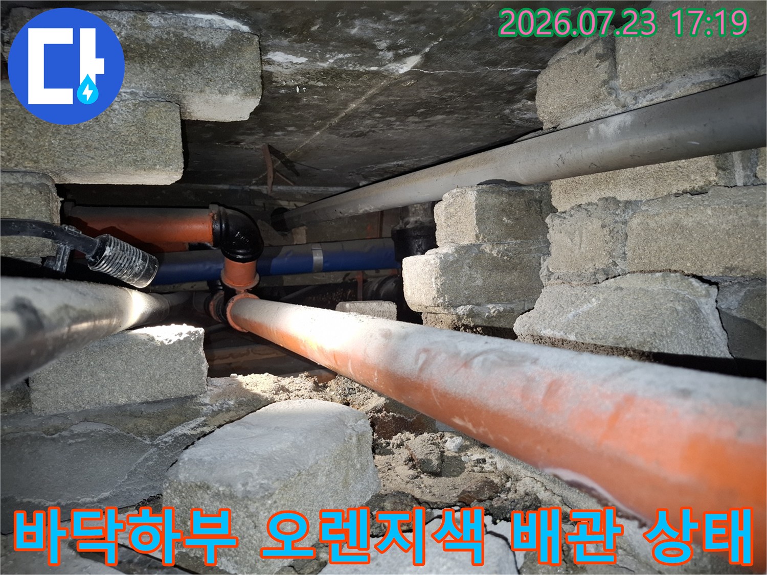 콘크리트 구조물 아래로 지나가는-오렌지색의-노후된-배관-연결부위