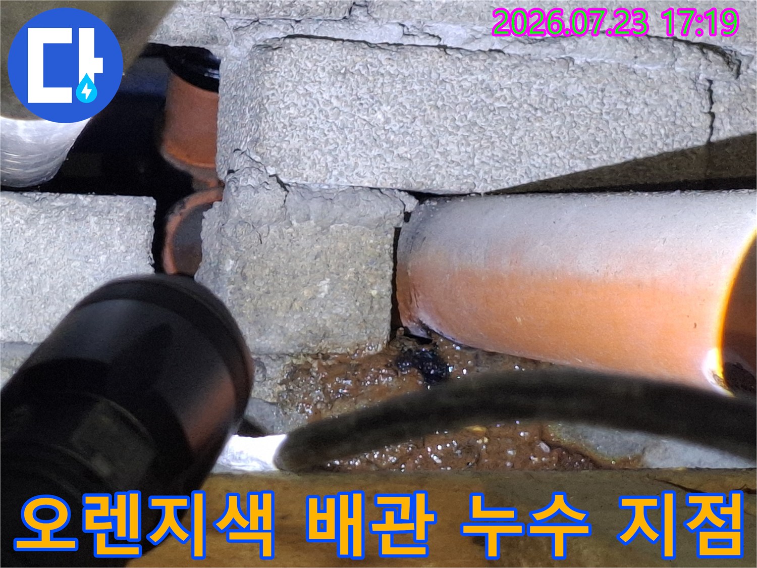 콘크리트 벽 하단에 위치한-부식이 심해 구멍 난 오렌지색 배관 사진