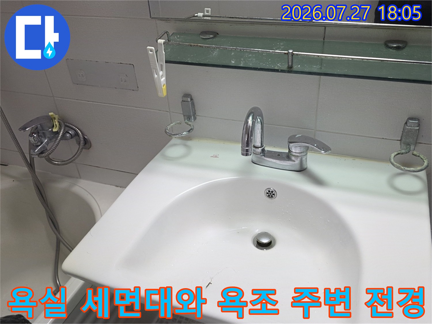흰색 세면대와 수전-옆으로 보이는 욕조와 샤워기-상단 거울 선반이 배치된 화장실 내부 모습