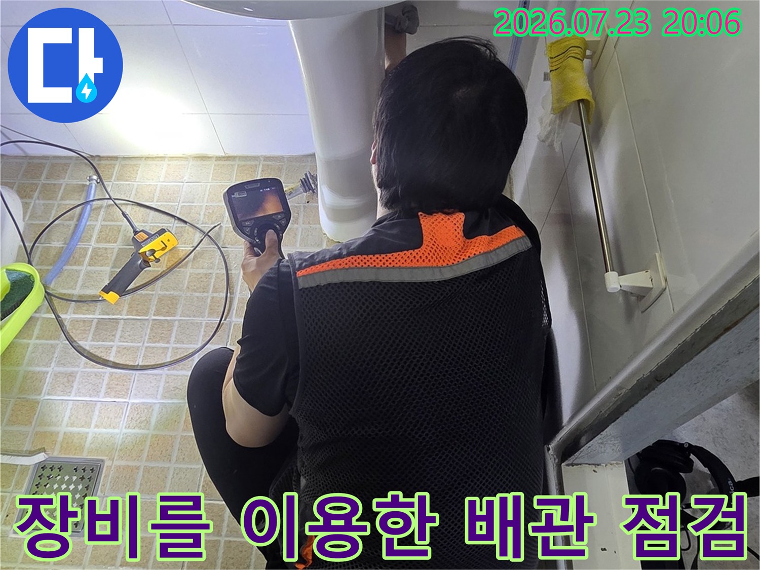작업자가 세면대 하단 바닥으로 이어지는 매립 배관을 정밀 장비로 탐지하는 모습