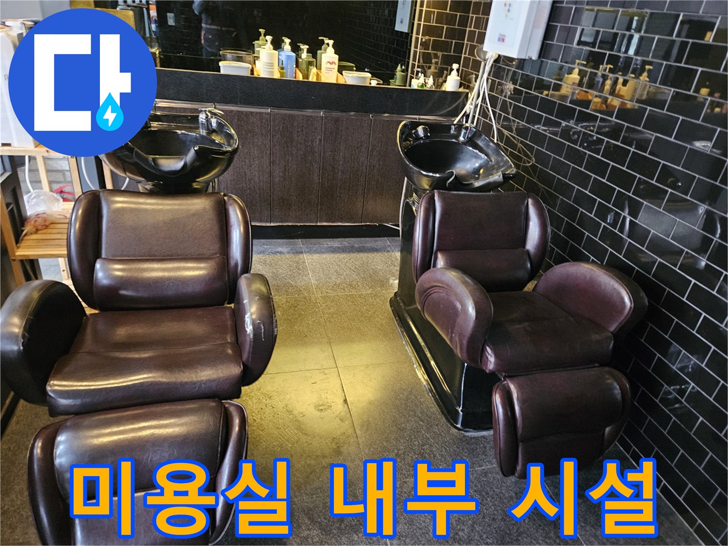 어두운 톤의 타일과 샴푸대 의자가 놓인 미용실 전경