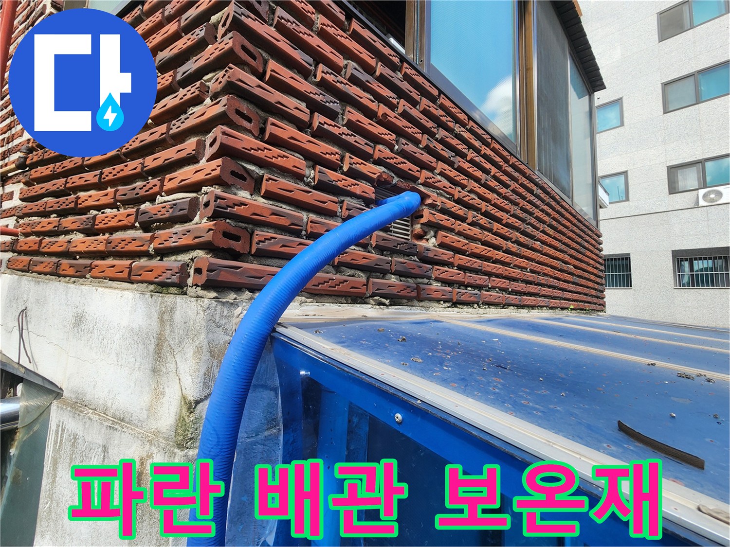 벽돌 건물 외벽에 연결된 파란색 배관 보호재