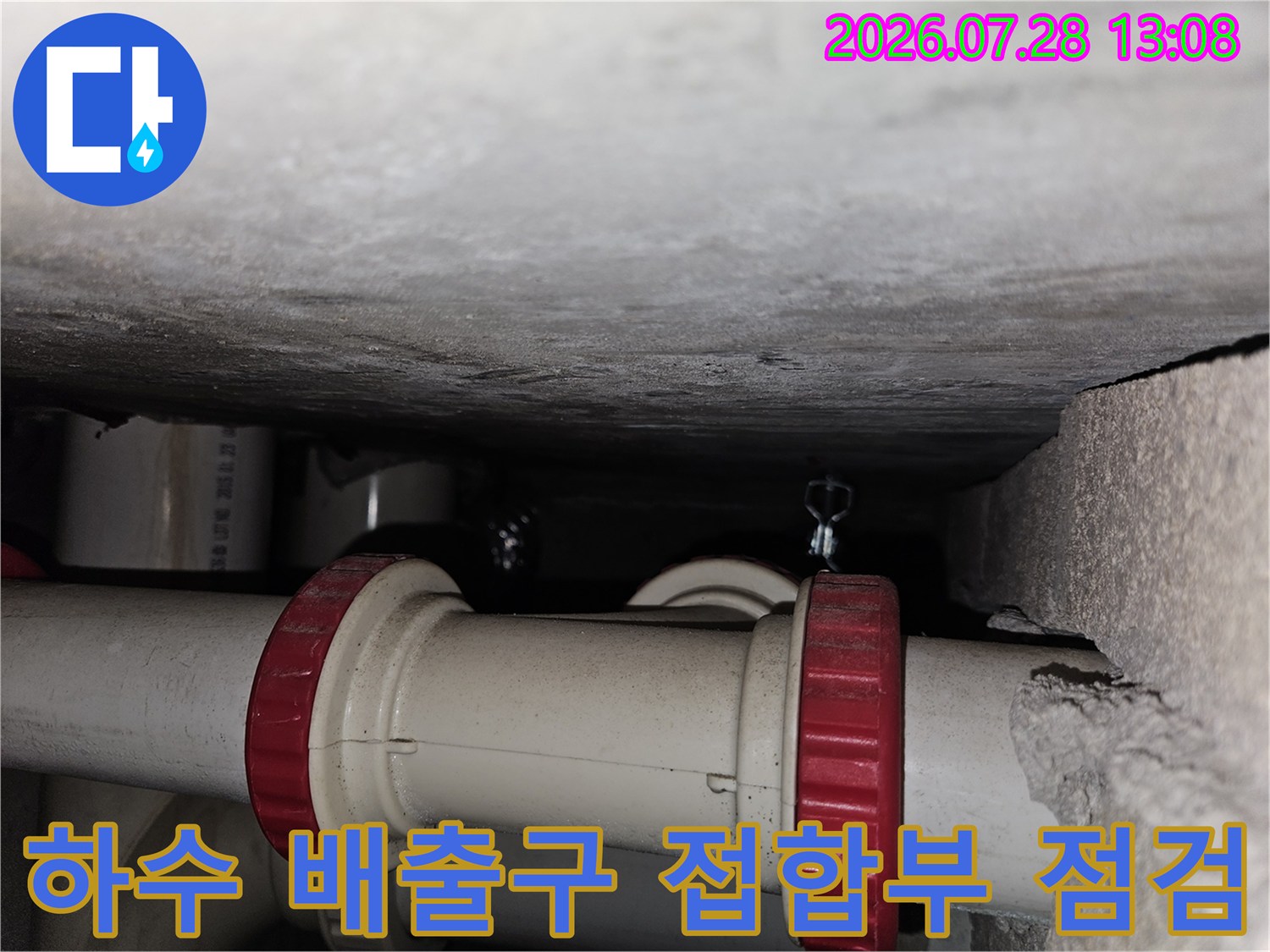 먼지 낀 공간 속 노출된 주방 배수 파이프의 연결 상태를 촬영한 사진