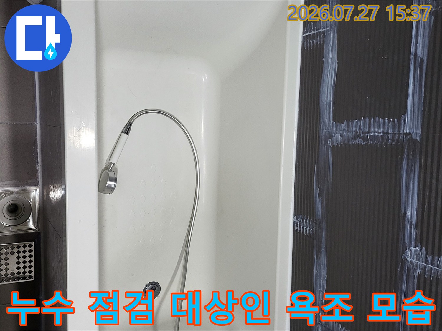 어두운 톤의 벽면 타일과 대비되는 흰색 욕조와 바닥 유가가 보이는 전경