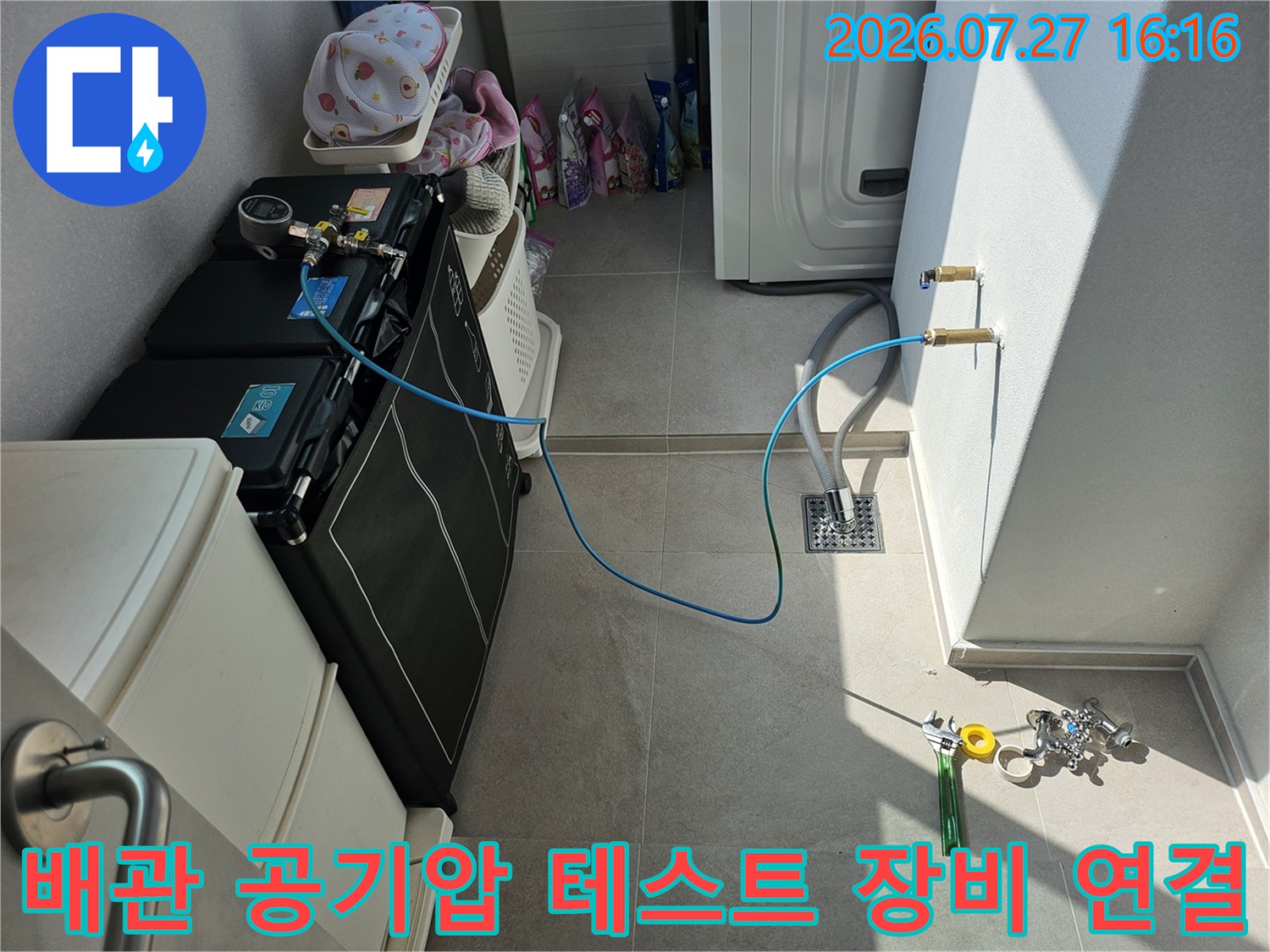 누수 점검을 위해 파란색 호스와 압력 측정 장비를 벽면 배관에 연결한 모습