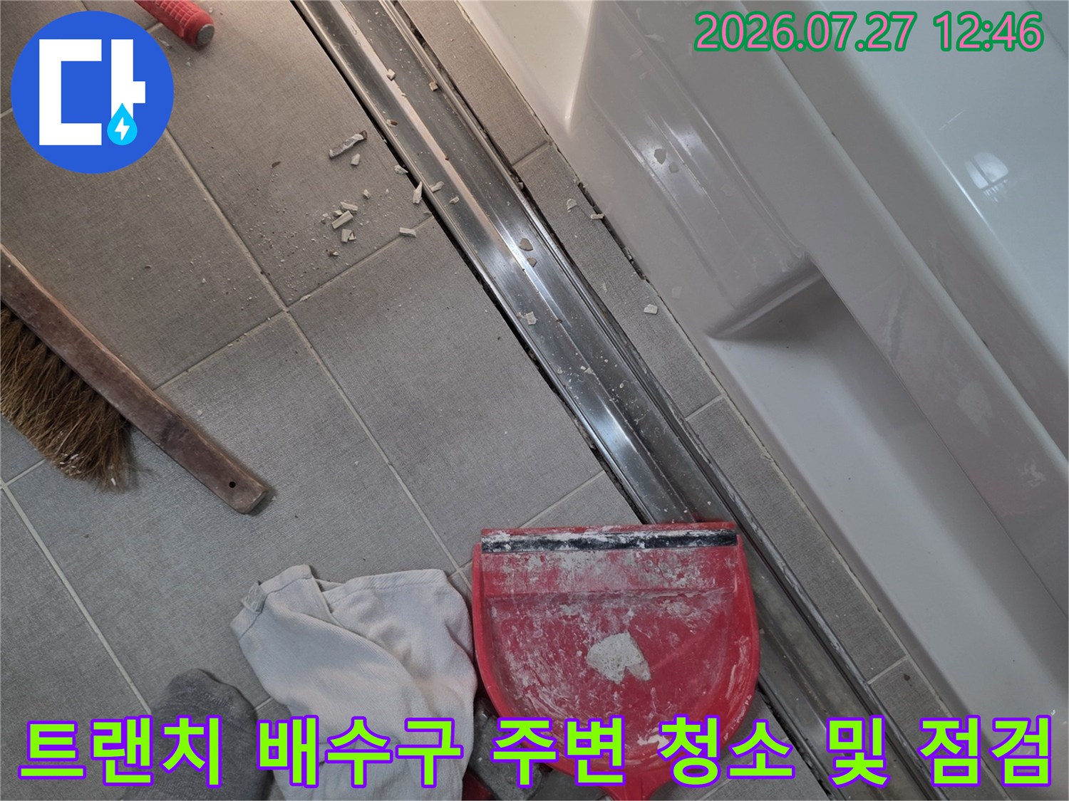 회색-타일-바닥의-긴-배수구-옆에-작업용-장갑과-청소도구가-놓여있는-현장-사진