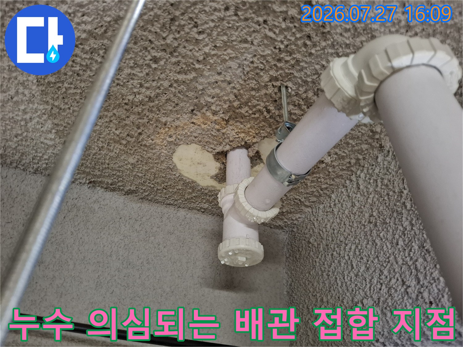 천장에 고정된 하얀색 배관의 연결 캡과 금속 고정 밴드가 보이는 사진