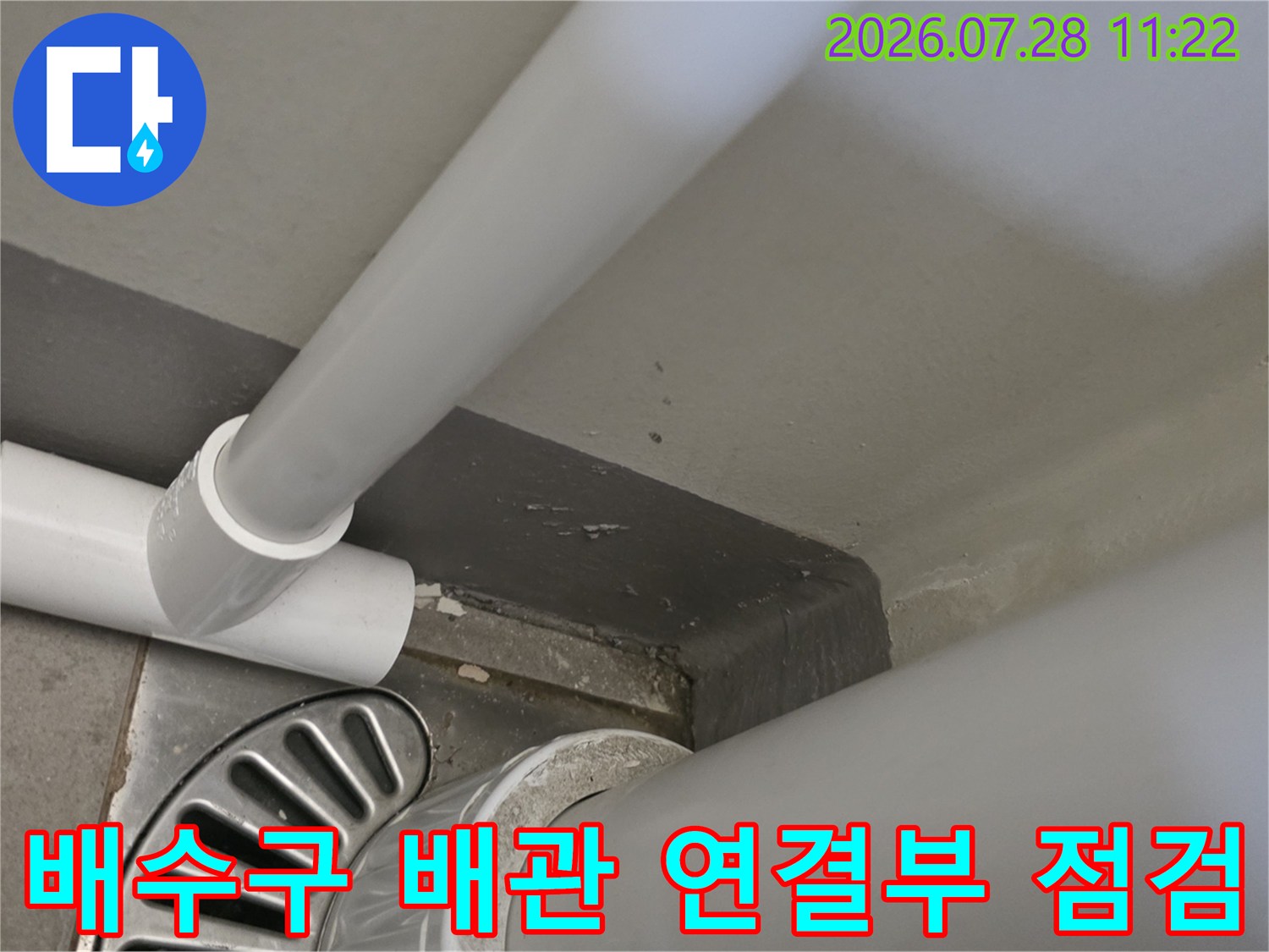 베란다 배수구 주변의 하얀색 배관 연결 부위와 바닥 유가 구조물