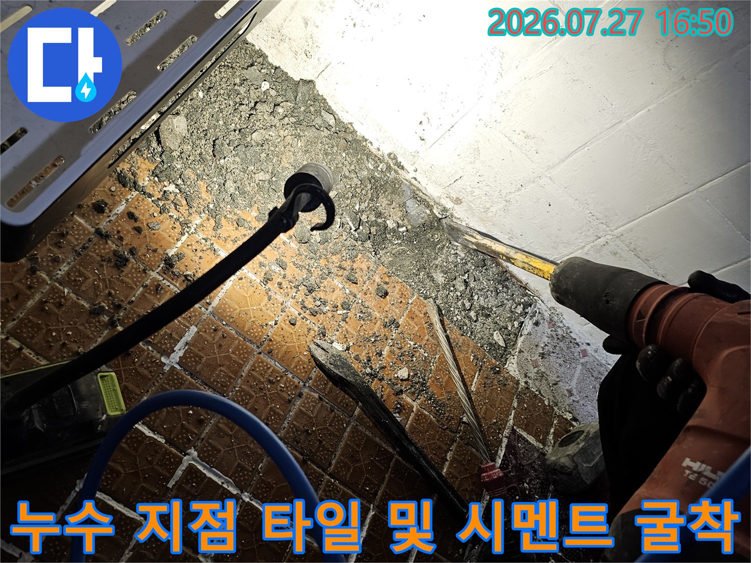 전동 드릴 장비와 파란색 호스가 연결된 현장에서 바닥을 굴착하는 모습