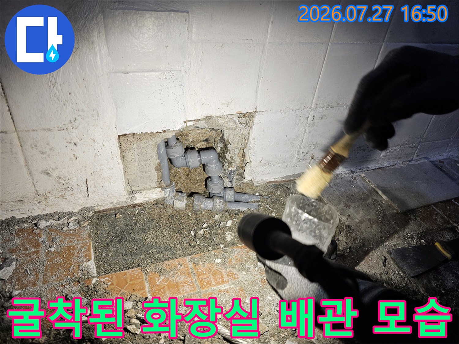 화장실 바닥 타일을 걷어내고 드러난 회색 플라스틱 배관-연결 부위-작업자의 손과 브러시