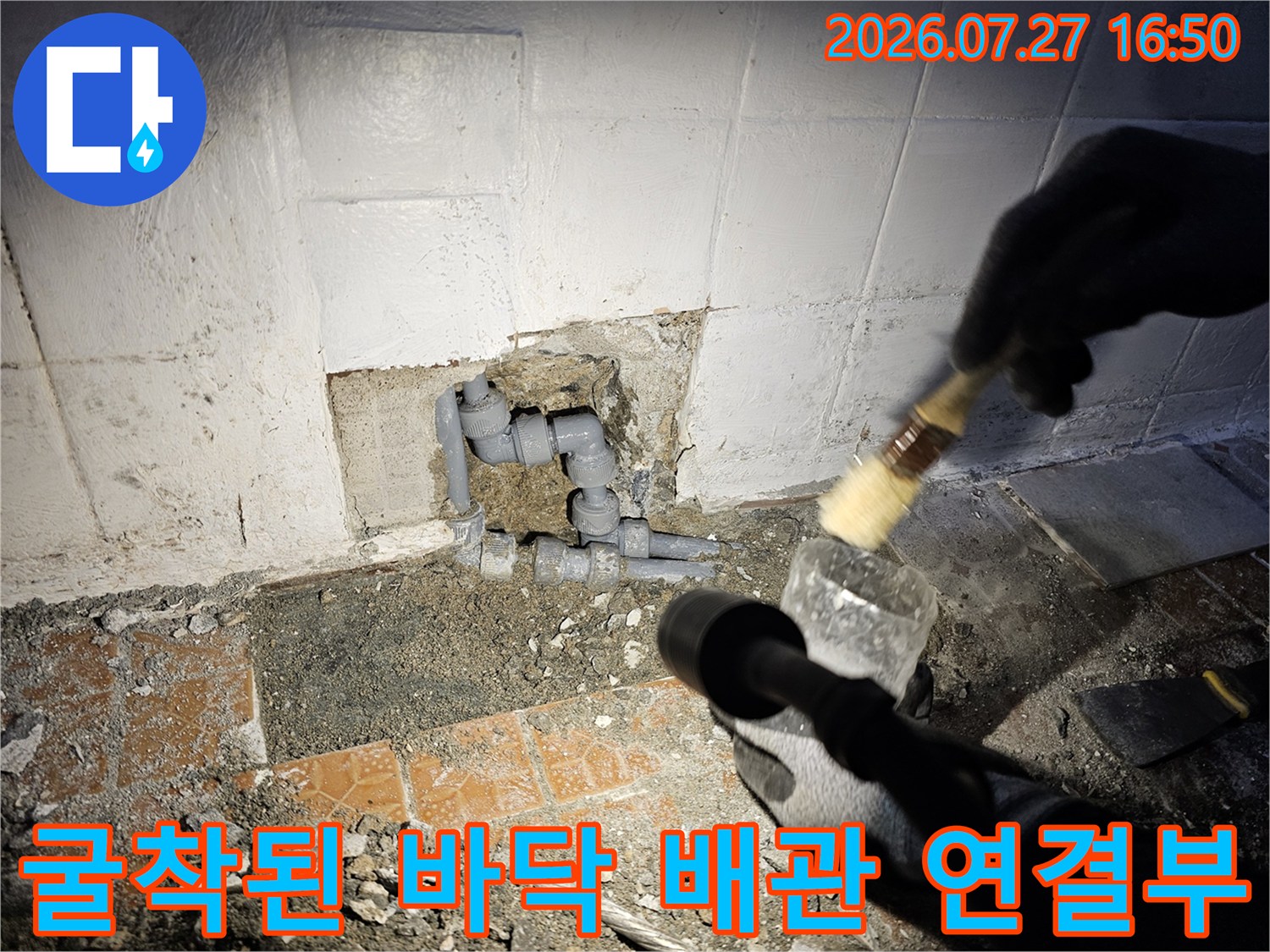 회색-배관-연결-부위와-그-주변의-시멘트-잔해물이-보이는-화장실-바닥-사진
