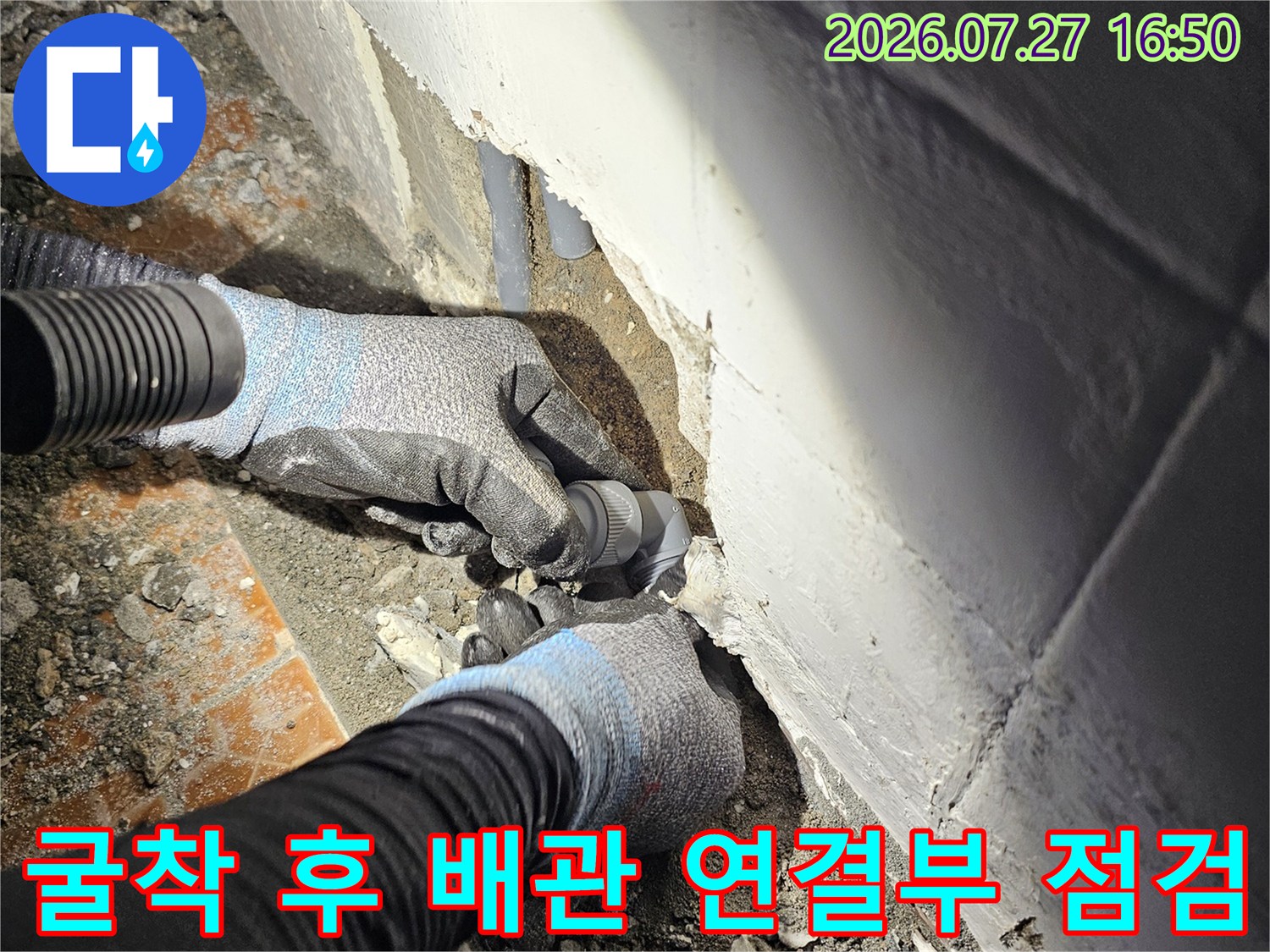 회색빛의 플라스틱 배관이 매립되어 있던 바닥면에서 노출되어 작업자의 손에 의해 확인되는 장면