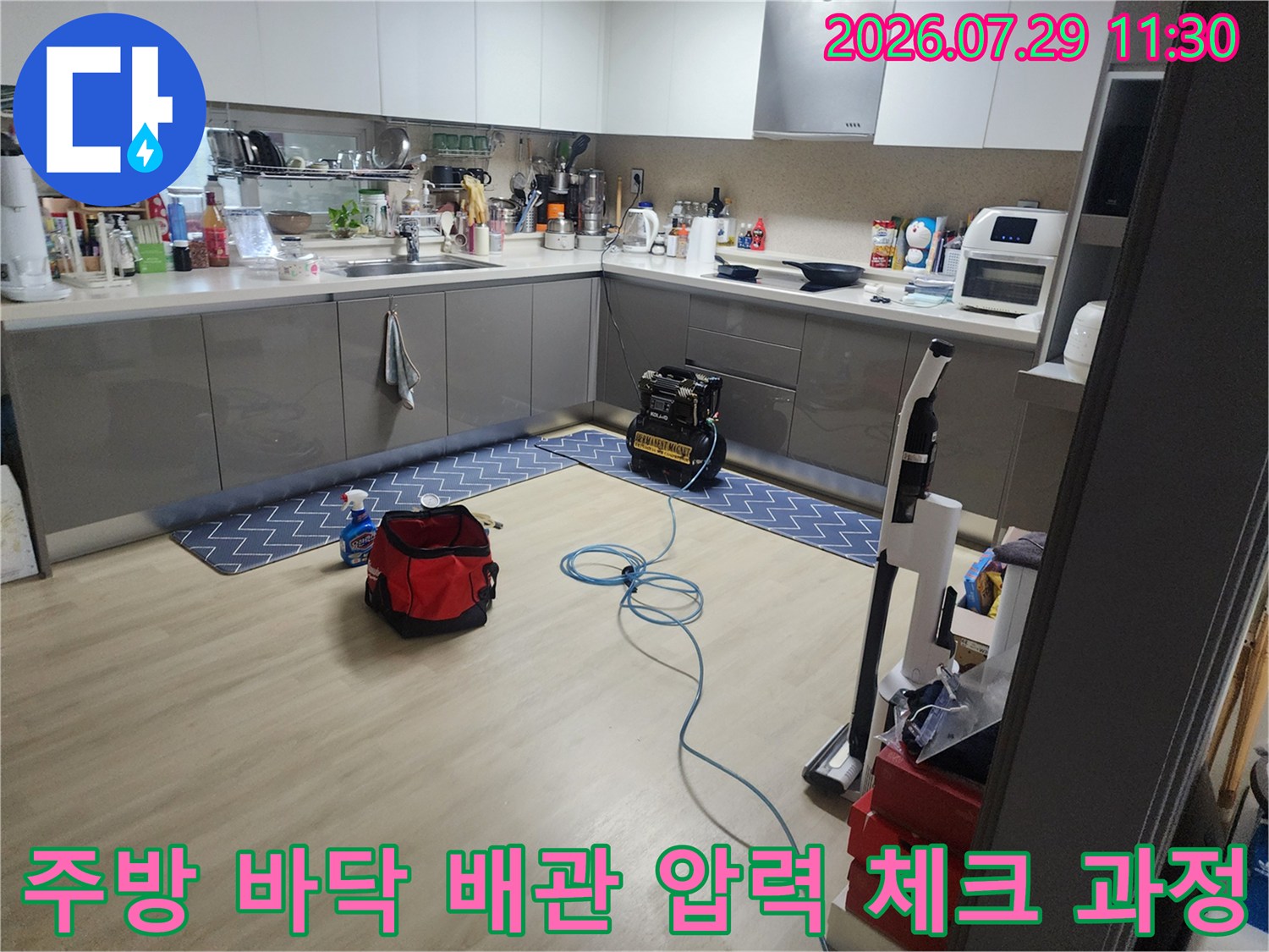 공압 테스트 장비와 연결된 호스를 사용하여 주방 배관의 이상 유무를 검사하는 장면