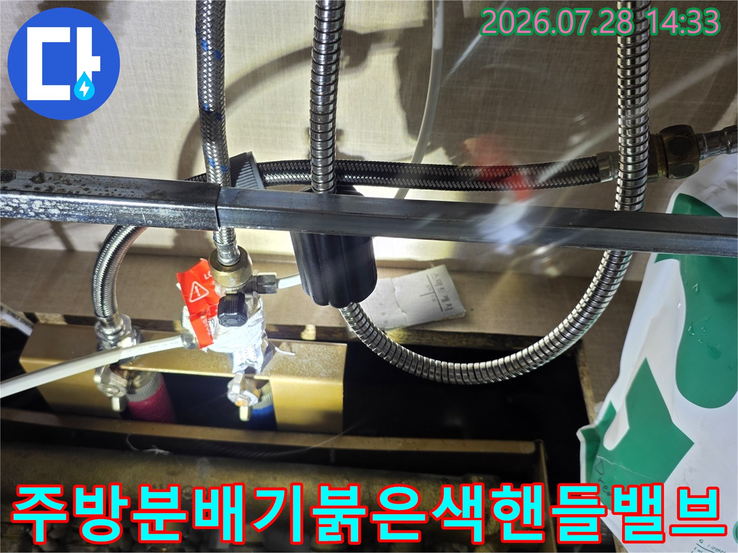 싱크대 하단 배관 분배기에 설치된 붉은색 제어 밸브와 연결된 금속 주름관 사진