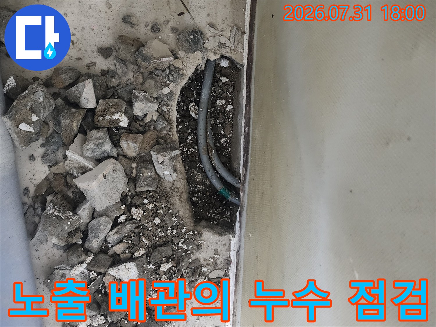 거친 질감의 바닥재를 파헤치고 드러난 회색 배관과 주변 자갈들