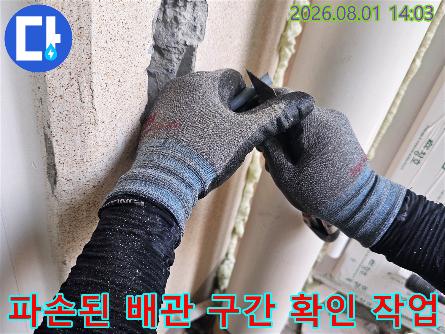 장갑을 낀 손으로 세탁실의 파손된 배관 구역을 면밀히 살피는 장면