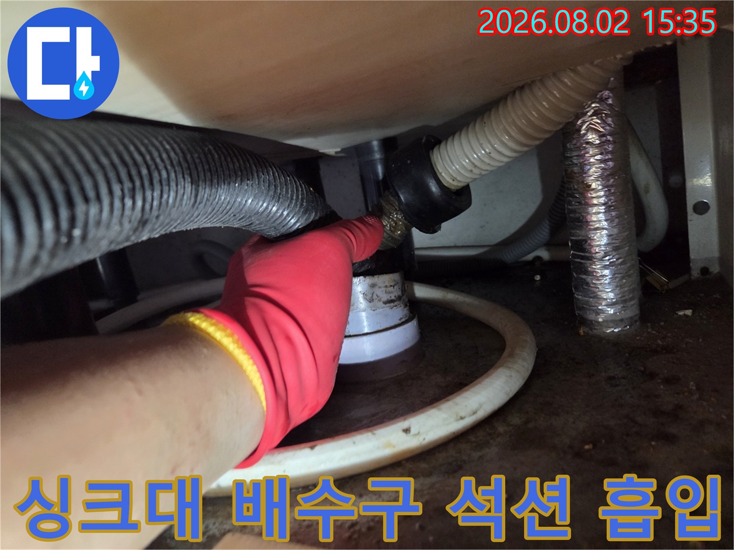 장갑을 낀 작업자가 싱크대 하단부 배출 경로에 석션 장비를 연결하여 이물질을 제거하는 과정