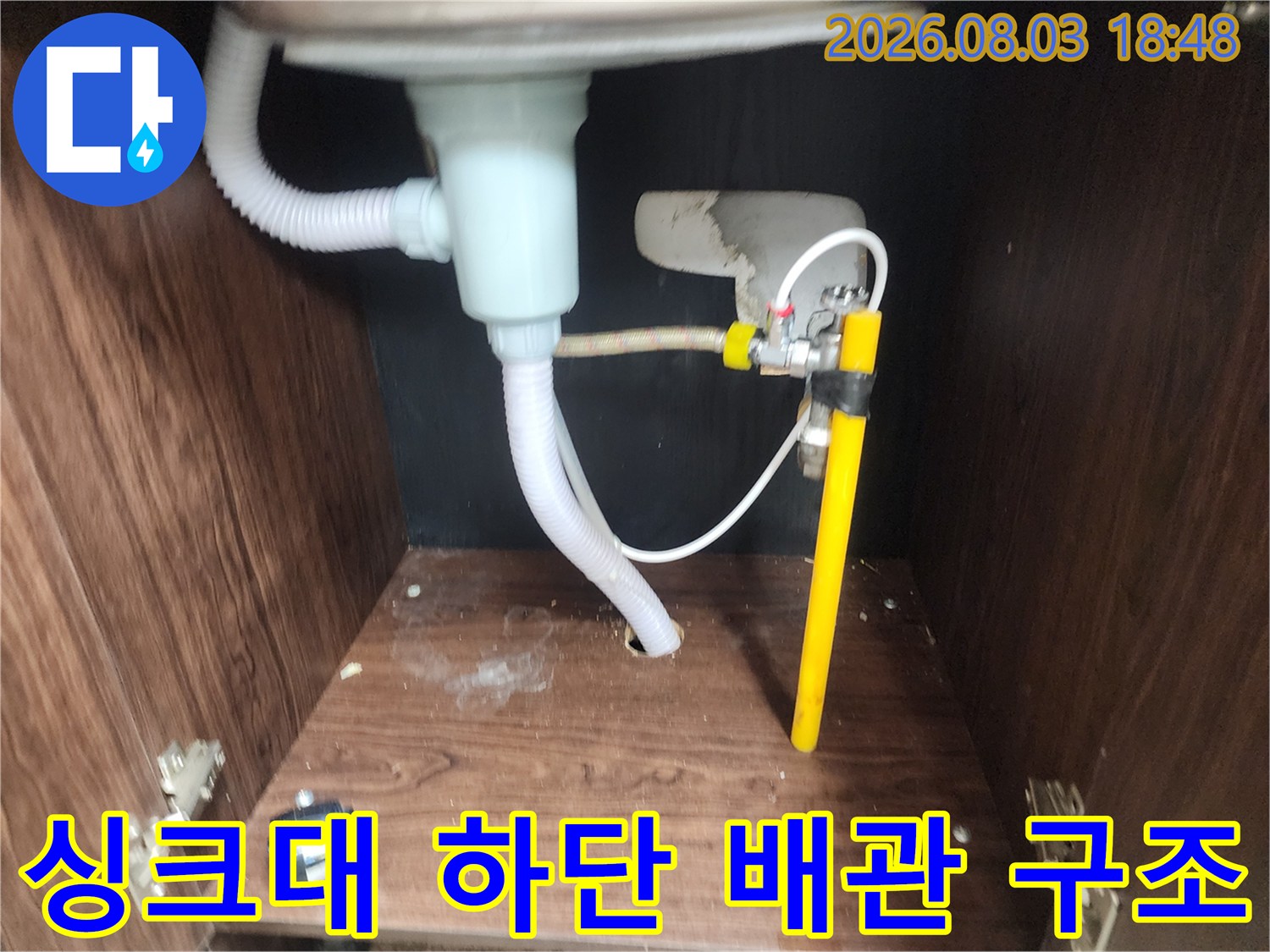 하얀색 호스와 노란색 관이 연결된 싱크대 밑 배관