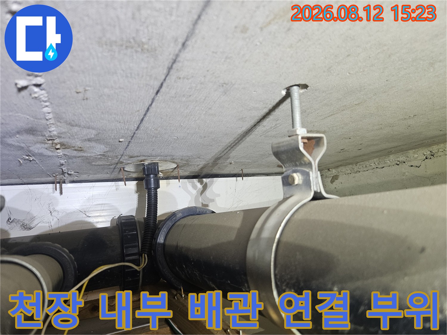 천장 슬라브 아래로 배치된 검은색 하수 배관과 지지 구조물-전경