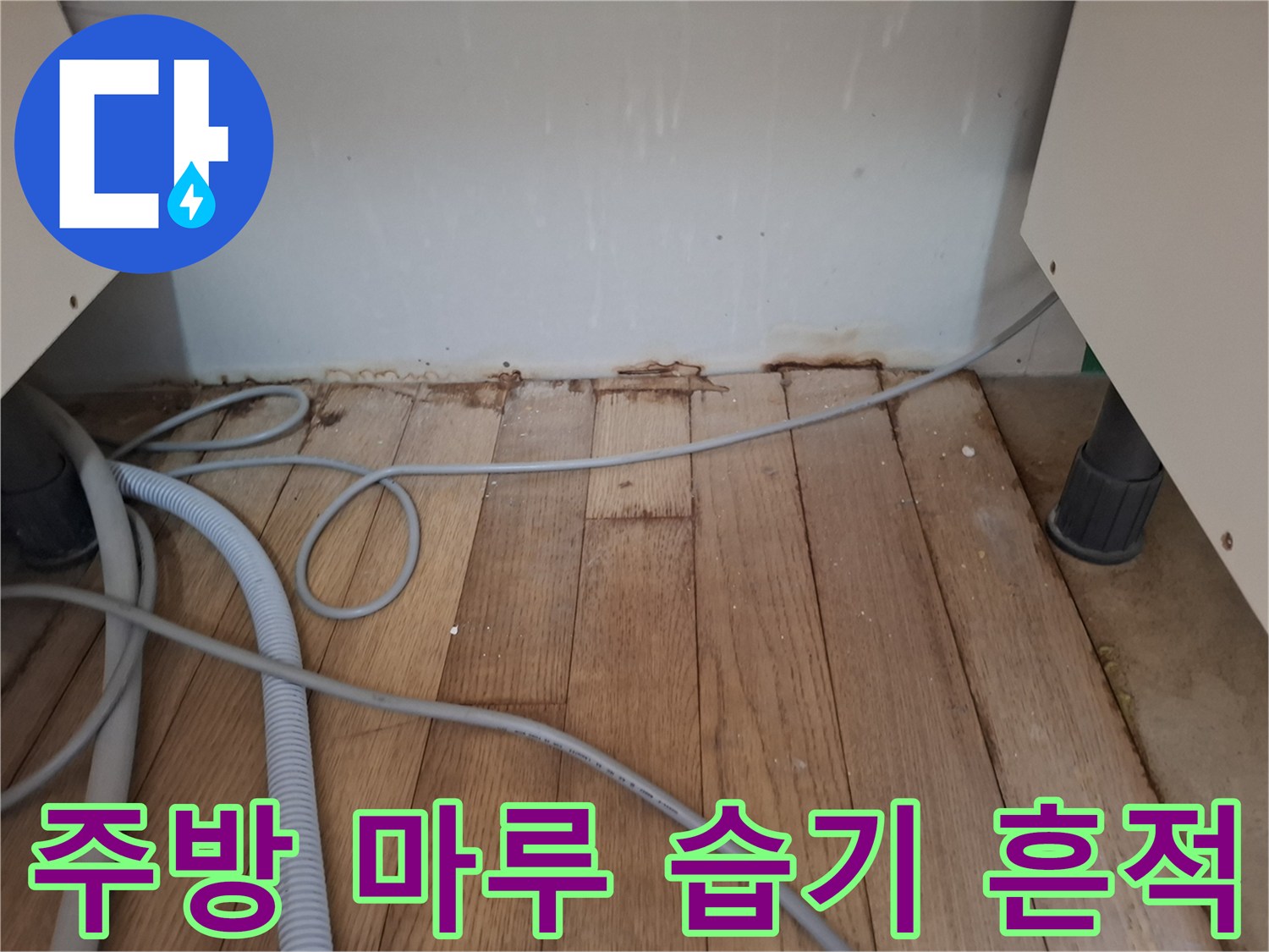 싱크대 하부장 근처 강화마루의 짙은 변색 부위와 배관 노출 상태