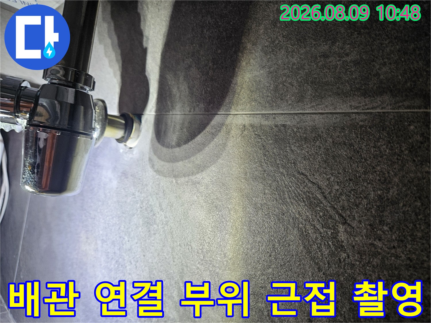 어두운 색상의 욕실 타일과 금속 배관 연결부의 상세 모습