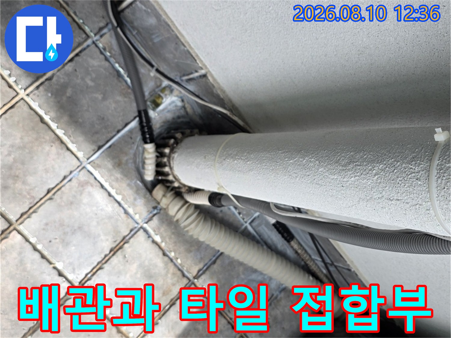 베란다 바닥 타일과 수직 배관의 경계 부분을 촬영한 사진입니다.