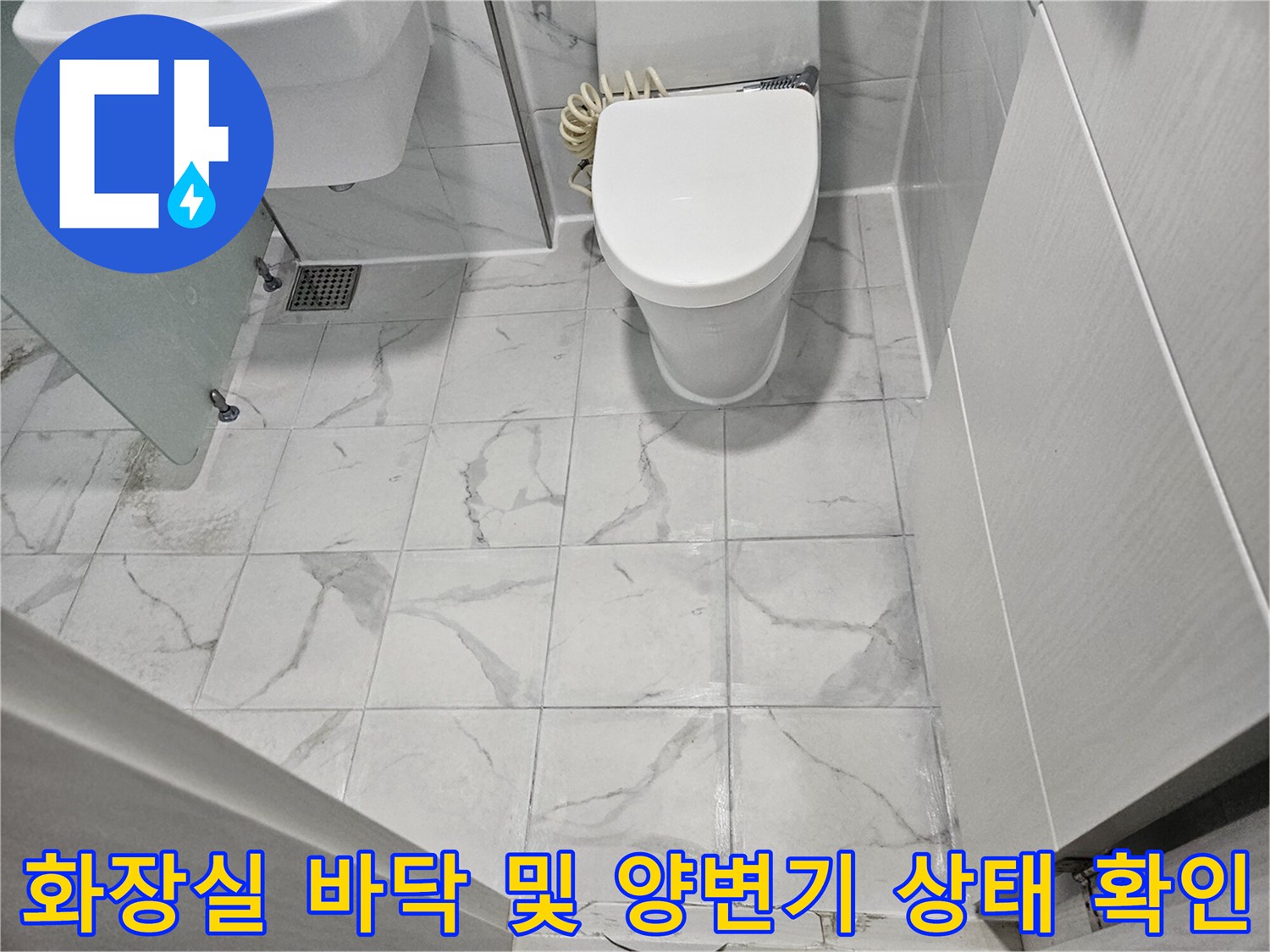 흰색 타일이 깔린 화장실-양변기와 세면대-배수구 유가가 보이는 바닥 전경