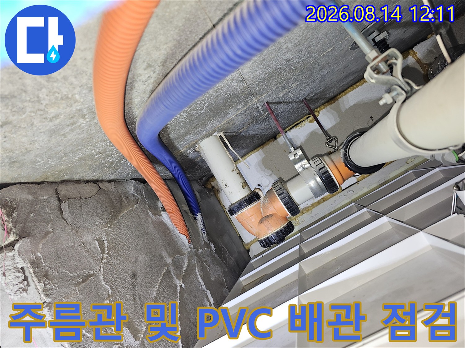 오렌지색 주름관과 파승색 호스가 연결된 천장 내부 배관의 누수 여부를 확인하는 장면입니다.