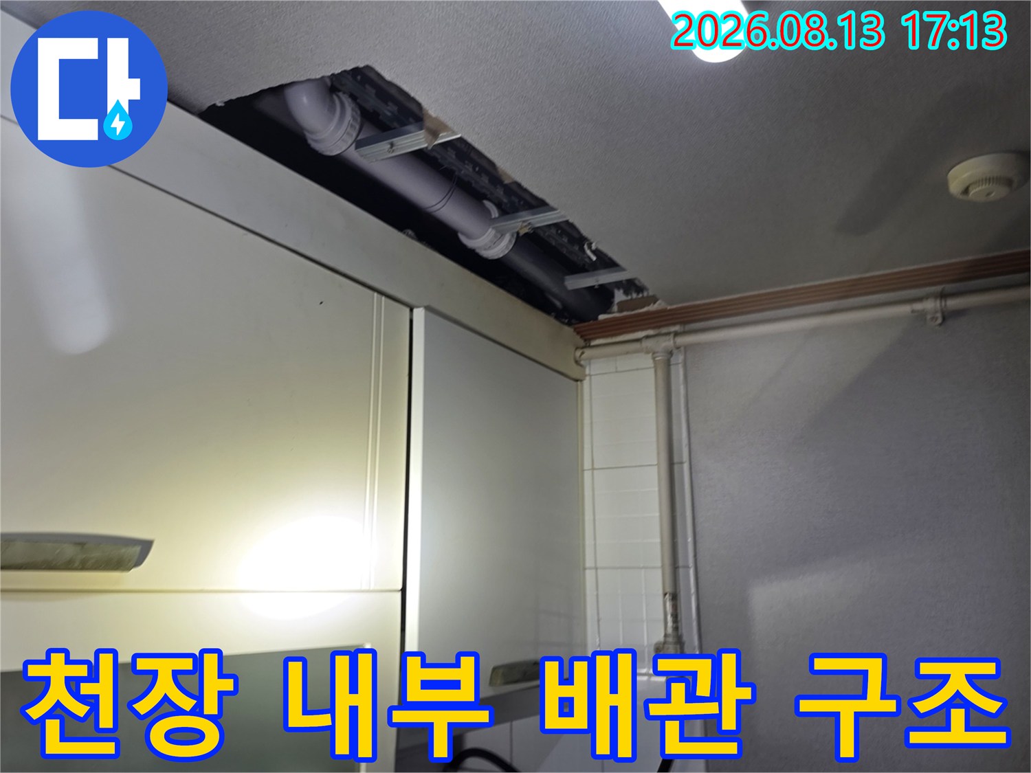 주방 상부장 뒤편 천장 내부에 노출된 배관들의 연결 부위 점검 사진입니다.