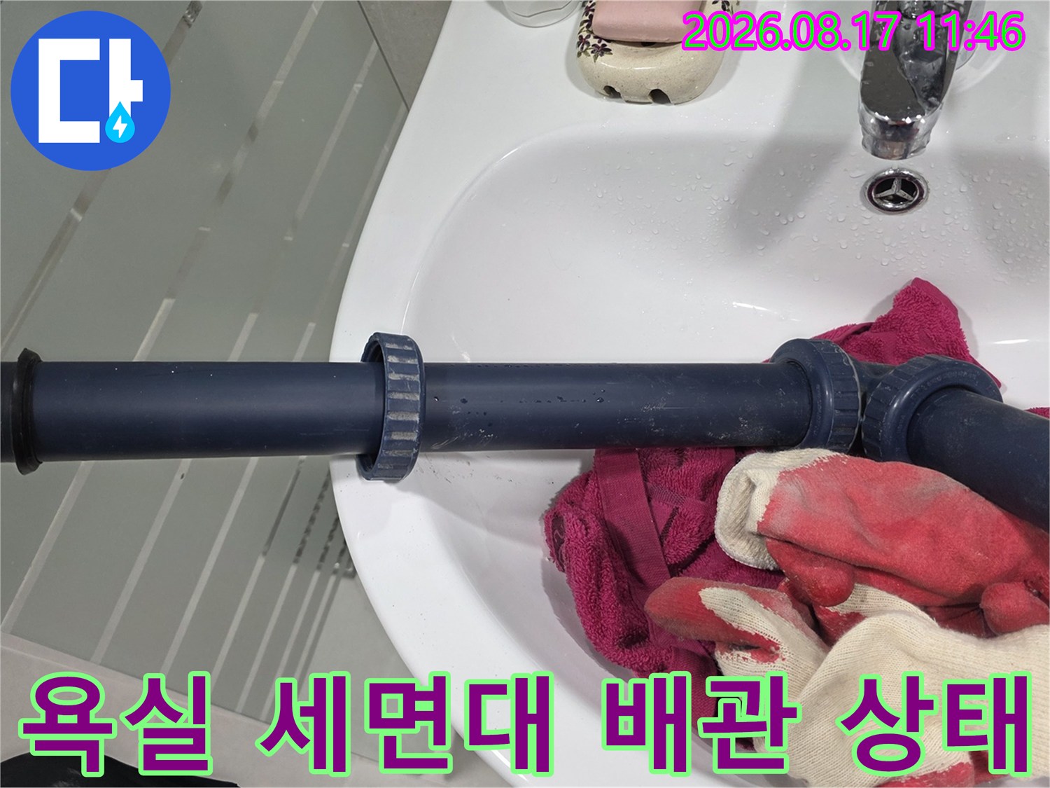 세면대 아래에 설치된 검은색 배관의 연결 부위를 촬영한 사진입니다.