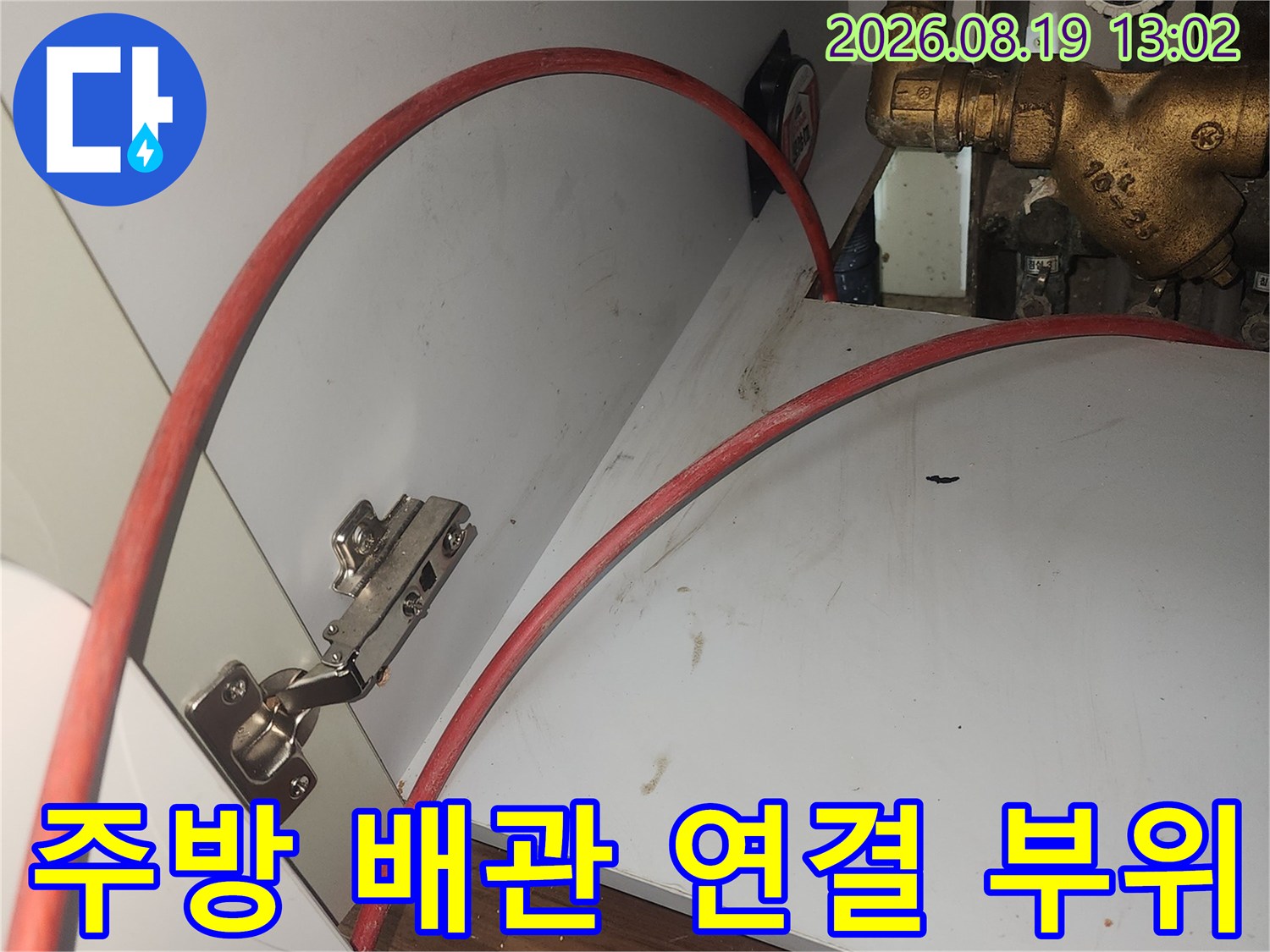 금속 밸브와 붉은색 호스가 설치된 싱크대 하부장 내부