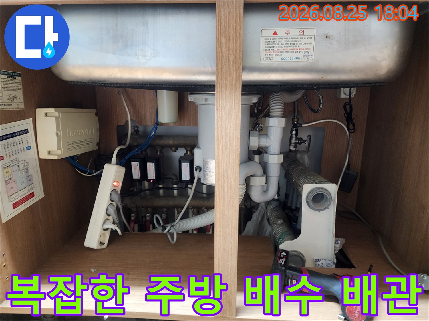 주방 하부장 내부에 노출된 각종 배수 호스와 전기 제어 장치 모습