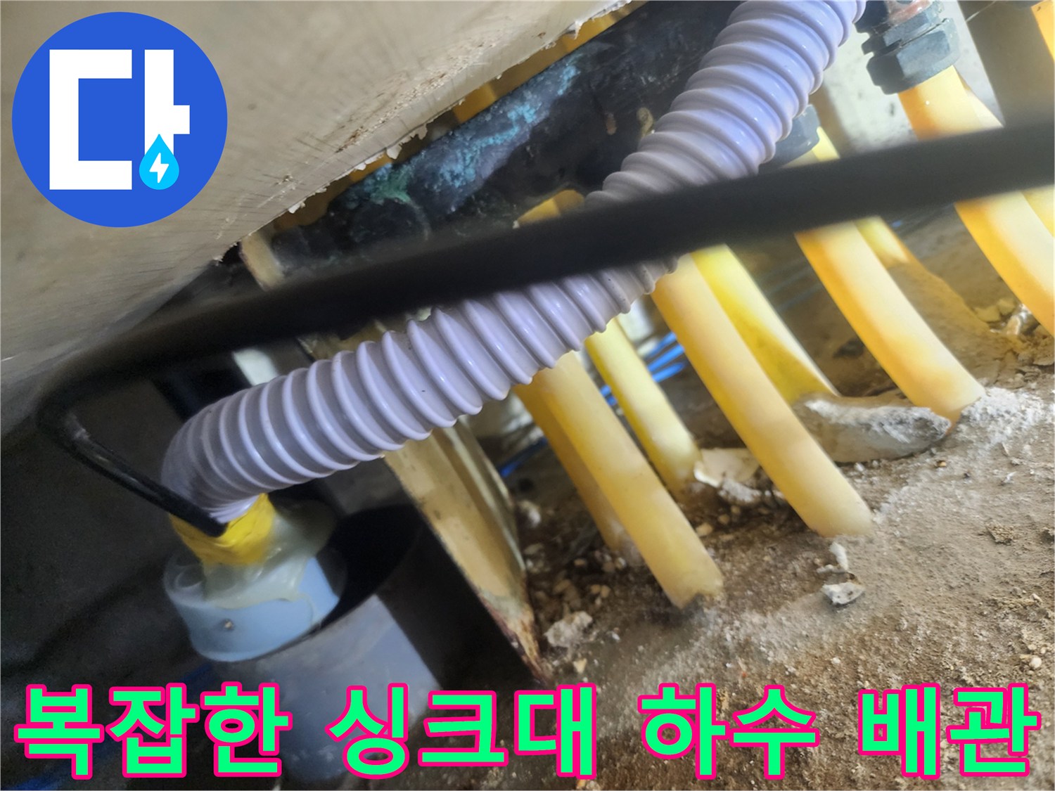 싱크대-하부장-내부의-복잡하게-얽힌-노란색-및-보라색-배관-상태