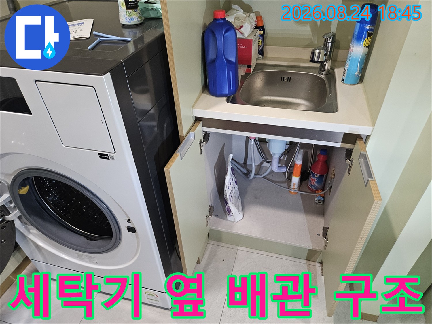 세탁기 하단 수납 공간에 배치된 다양한 세정제와 배관 호스