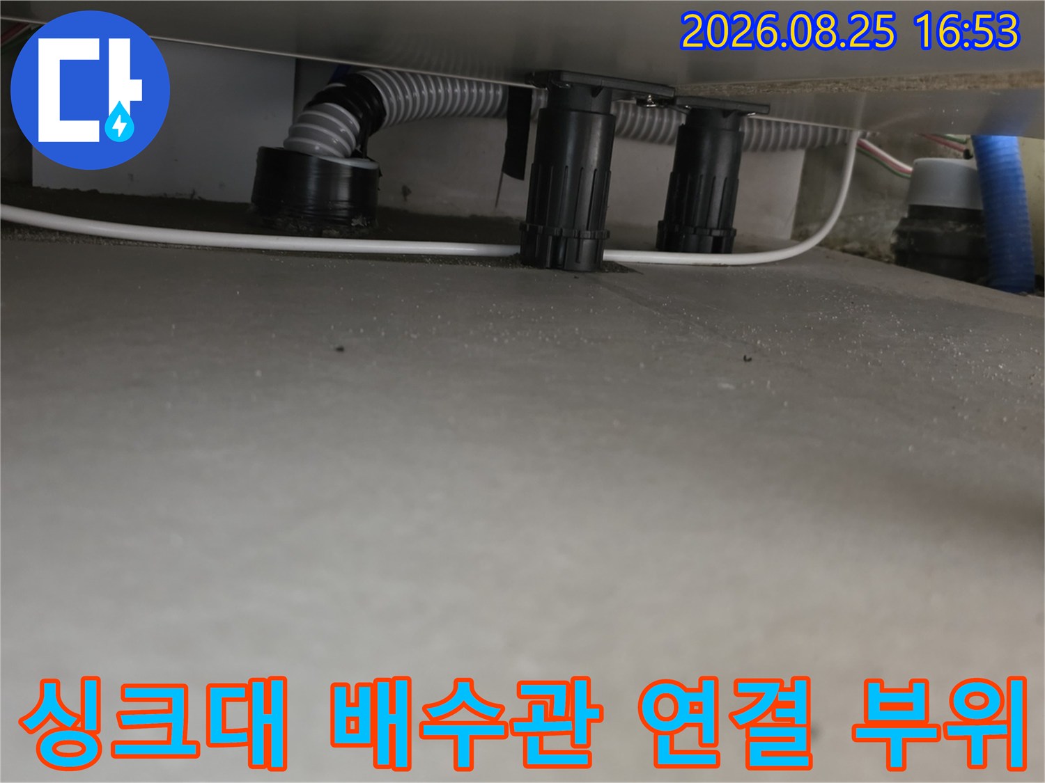 싱크대 하부의 검은색 배관 부품과 주름진 호스 연결 상태를 보여줍니다.