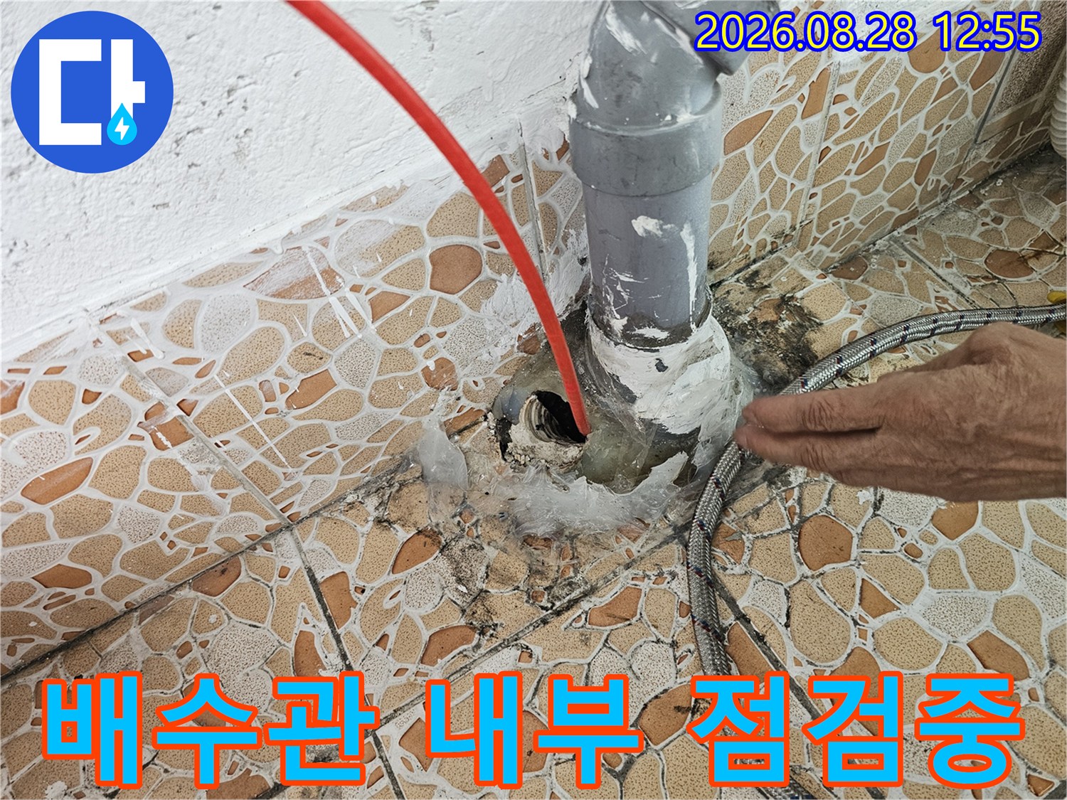 분해된 배관 입구와 타일 틈새로 내시경 장비를 삽입하여 검사하는 모습입니다.